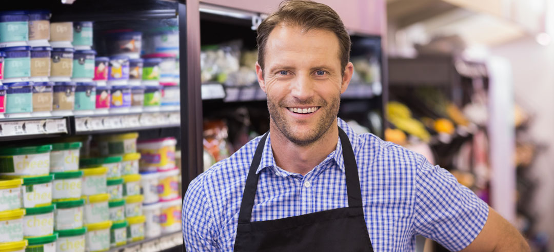 Trabajador de un supermercado sonriendo con yogures de fondo